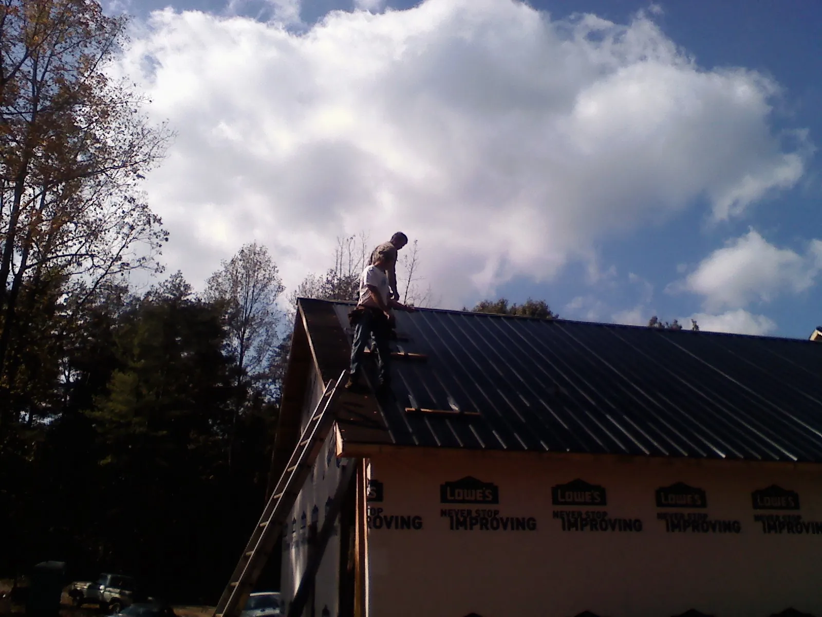Roofer fastening dark metal panels high against a cloudy sky, from a Roof Inspection job in Caledonia